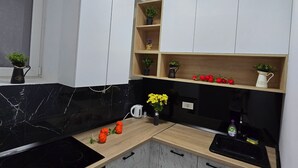 Et moderne køkken med bordplade i sort, hvide skabe, en indbygget ovn og en lille vask.