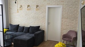 En moderne stue med en murstensvæg, en sofasæt, et sofabord i glas og en lænestol.