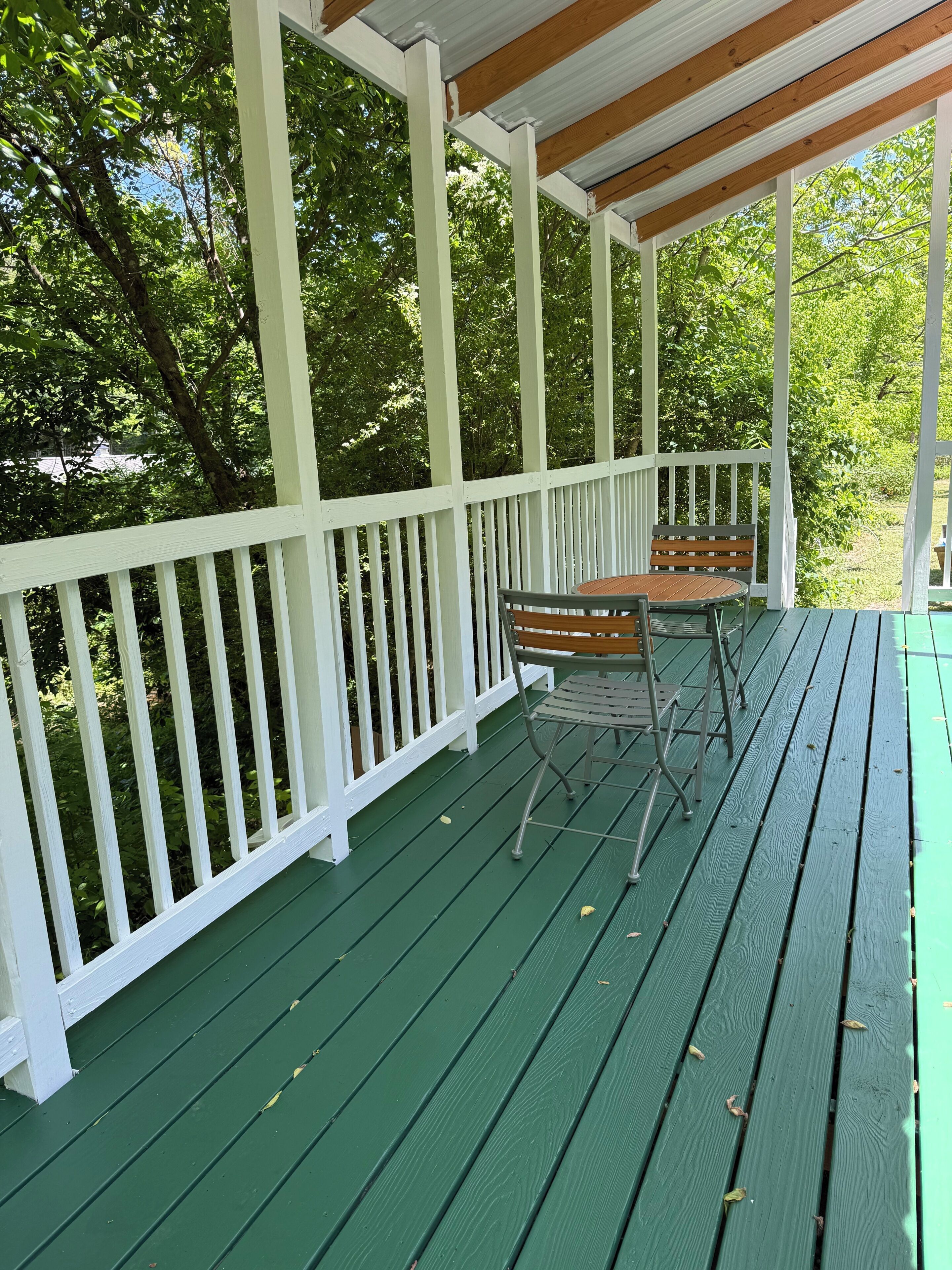 Een overdekte veranda met een groene vloer, witte leuningen en een tafel met stoelen.