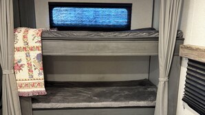 Un llit superposat amb un televisor a dalt, cortines i una manta amb un disseny.