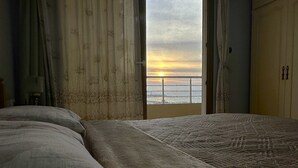 Ein Zimmer mit Bett, Fenster und Blick auf den Sonnenuntergang über dem Meer.