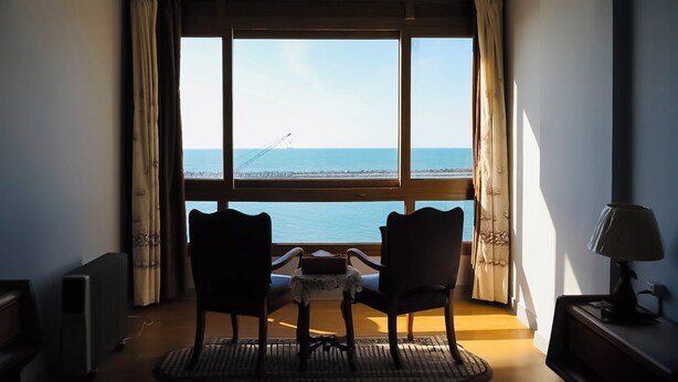 Ein Zimmer mit einem großen Fenster, zwei Stühlen, einem kleinen Tisch und einer Lampe.
