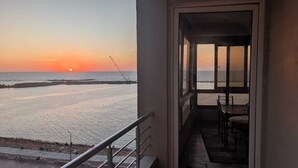 Ein Balkon mit Blick auf den Sonnenuntergang über dem Wasser, einer Mole und einem Tisch mit Stühlen.