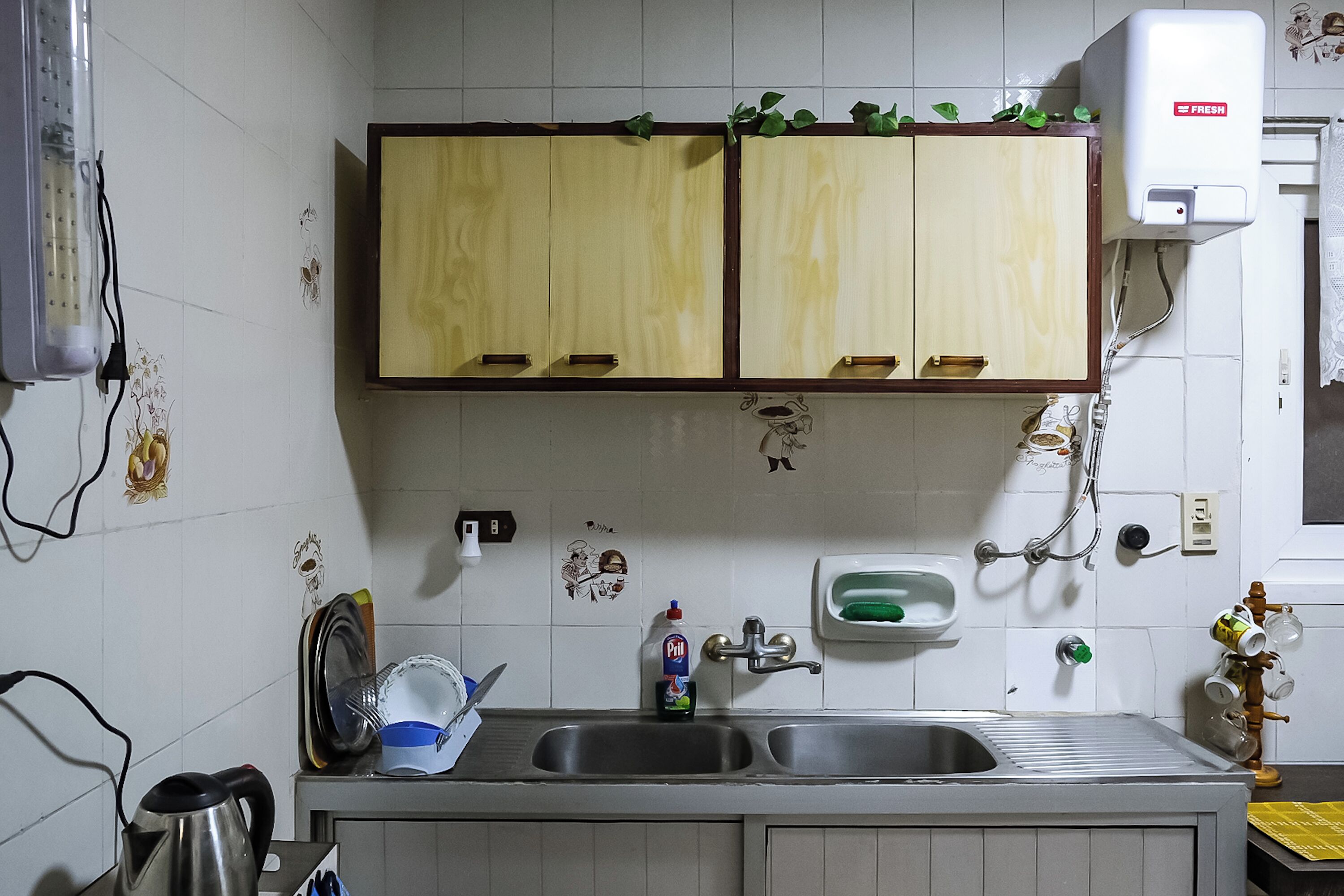 Een keuken met een dubbele spoelbak, houten kastjes, een afdruiprek en een waterdispenser.