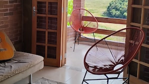 Una habitación con pared de ladrillo, puerta de madera que da a un balcón, una silla roja, una guitarra y una alfombra estampada.