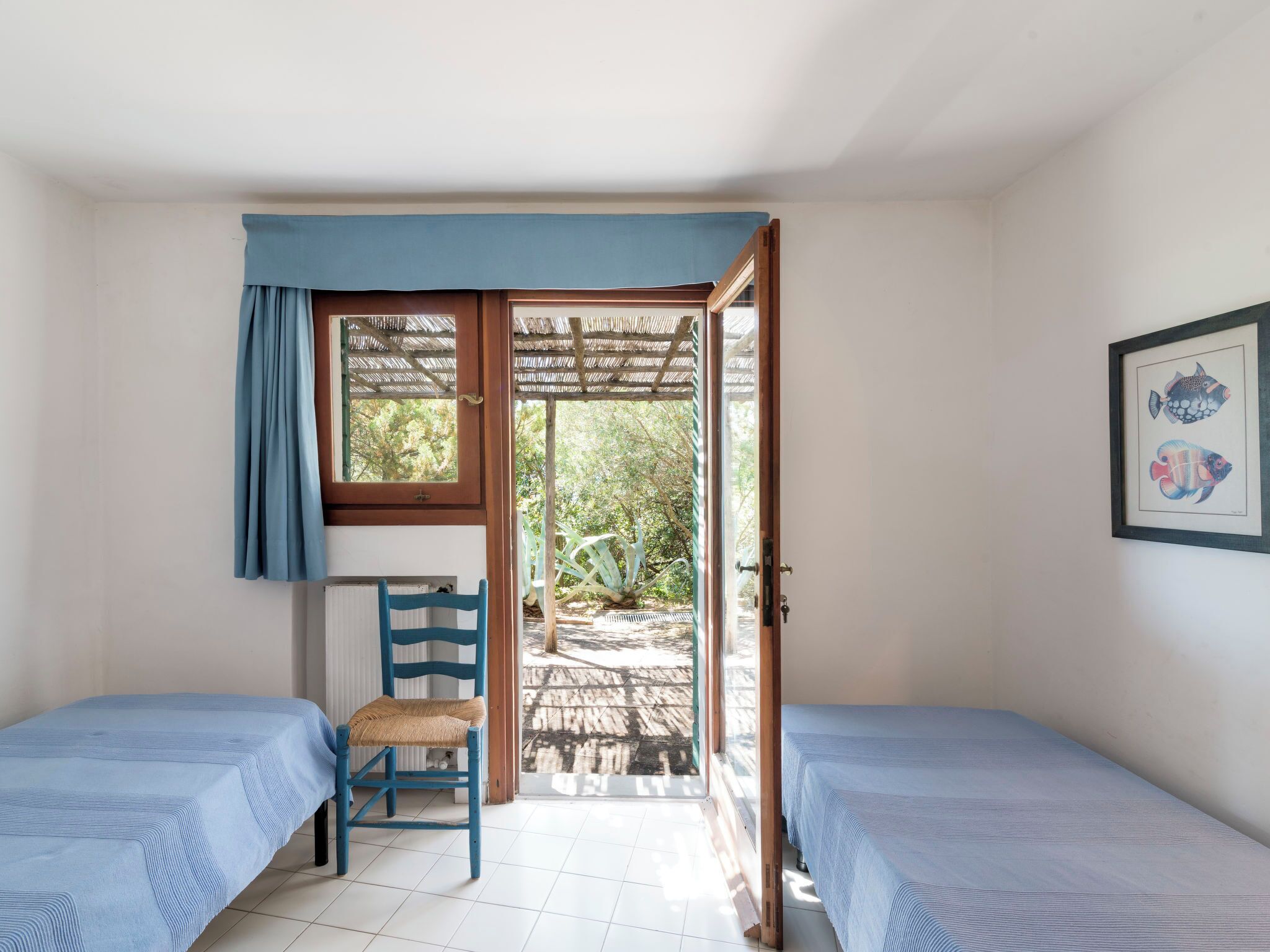 A room with two beds, a chair, a window with a curtain, and a door leading outside.
