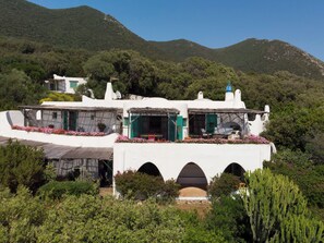 A white building with multiple balconies, arched doorways, and a mountainous backdrop.