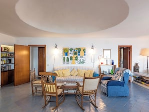 A living room with a sofa, chairs, a bookshelf, a painting, and a lamp.