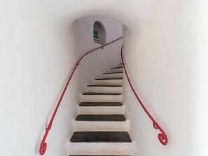 Un escalier avec une rampe rouge menant à une petite fenêtre en arc de cercle située en haut.