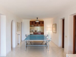 A spacious hallway with a ping pong table, a kitchen with wooden cabinets, and a tiled floor.