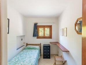 A small bedroom with a bed, a dresser, a chair, a window, and a mirror.