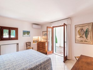 Une chambre à coucher comprenant un lit, une commode, une chaise, un radiateur et une porte donnant sur un espace extérieur.