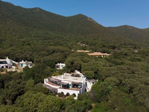 A white building with a flat roof surrounded by dense green forest and hills in the background.