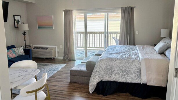 A bedroom with a bed, a desk, a chair, a standing lamp, a heater, and a view of the outside. - Beautiful Studio Apartment With King Sized Bed Just Blocks From the Beach! (Bethany Beach)