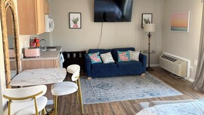 A modern living room with a TV, sofa, and dining area. - Beautiful Studio Apartment With King Sized Bed Just Blocks From the Beach! (Bethany Beach)
