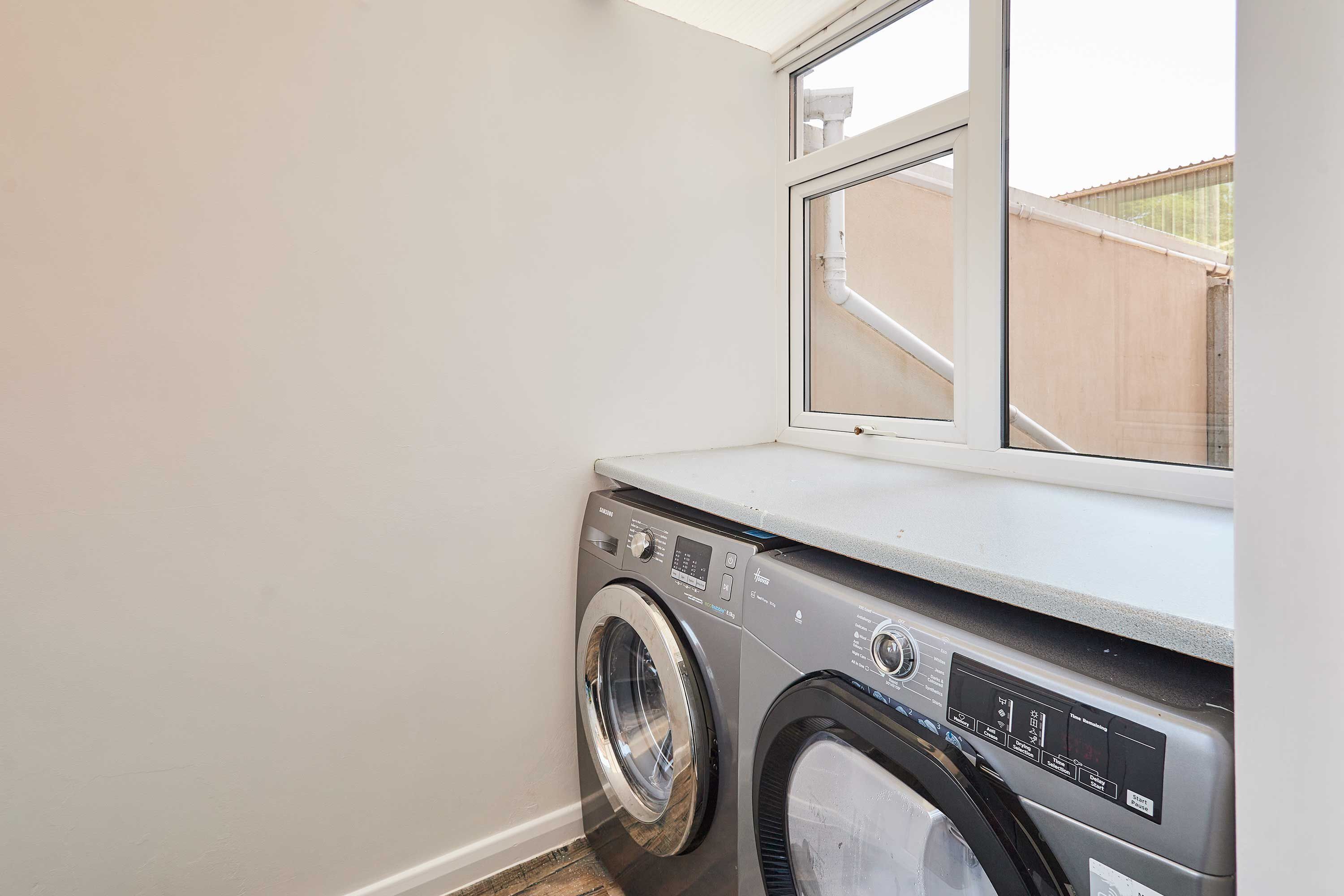 A compact laundry area with a washing machine and dryer, a window, and a view of a fence outside.