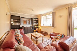 A living room with a sofa, a wooden coffee table, a bookshelf, a mirror, and a window with curtains.