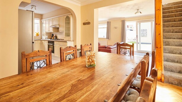 Een eetgedeelte met een houten tafel en stoelen, een keuken op de achtergrond en een trap.