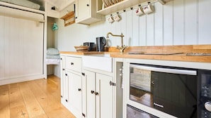 A kitchen with white cabinets, a wooden countertop, a built-in oven, and a hanging mug rack. - Host Stay Shepherds Delight (Harleston)