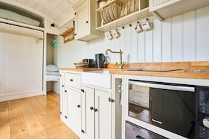 A kitchen with white cabinetry, a wooden countertop, a built-in oven, and a hanging rack with dishes. - Host Stay Shepherds Delight (Harleston)