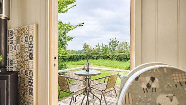 A room with a patterned wall, a round table with chairs, and a view of a garden. - Host Stay Shepherds Delight (Harleston)
