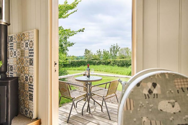 A room with a patterned wall, a round table with chairs, and a view of a garden. - Host Stay Shepherds Delight (Harleston)