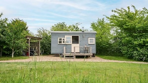 A small, single-story cabin with a porch, surrounded by a grassy field and trees. - Host Stay Shepherds Delight (Harleston)