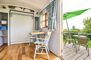 A room with a wooden floor, a bed with a white headboard, a table with chairs, a window with curtains, and a balcony with chairs and a green umbrella. - Host Stay Shepherds View (Harleston)