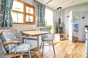 A cozy kitchen with a wooden table, two patterned chairs, a stove, and a window with curtains. - Host Stay Shepherds View (Harleston)