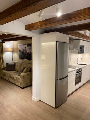 Eine moderne Küche mit integriertem Kühlschrank, Backofen und Spüle, Holzbalken an der Decke und einem Sofa im angrenzenden Wohnbereich.