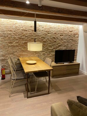 Ein Essbereich mit Holztisch, Stühlen, einem Fernseher auf einer Holzkommode und einer Wand aus Stein.