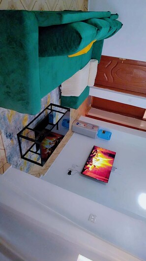 Quarto com manta verde, uma pintura, um armário de madeira e uma pequena mesa com um objeto azul.