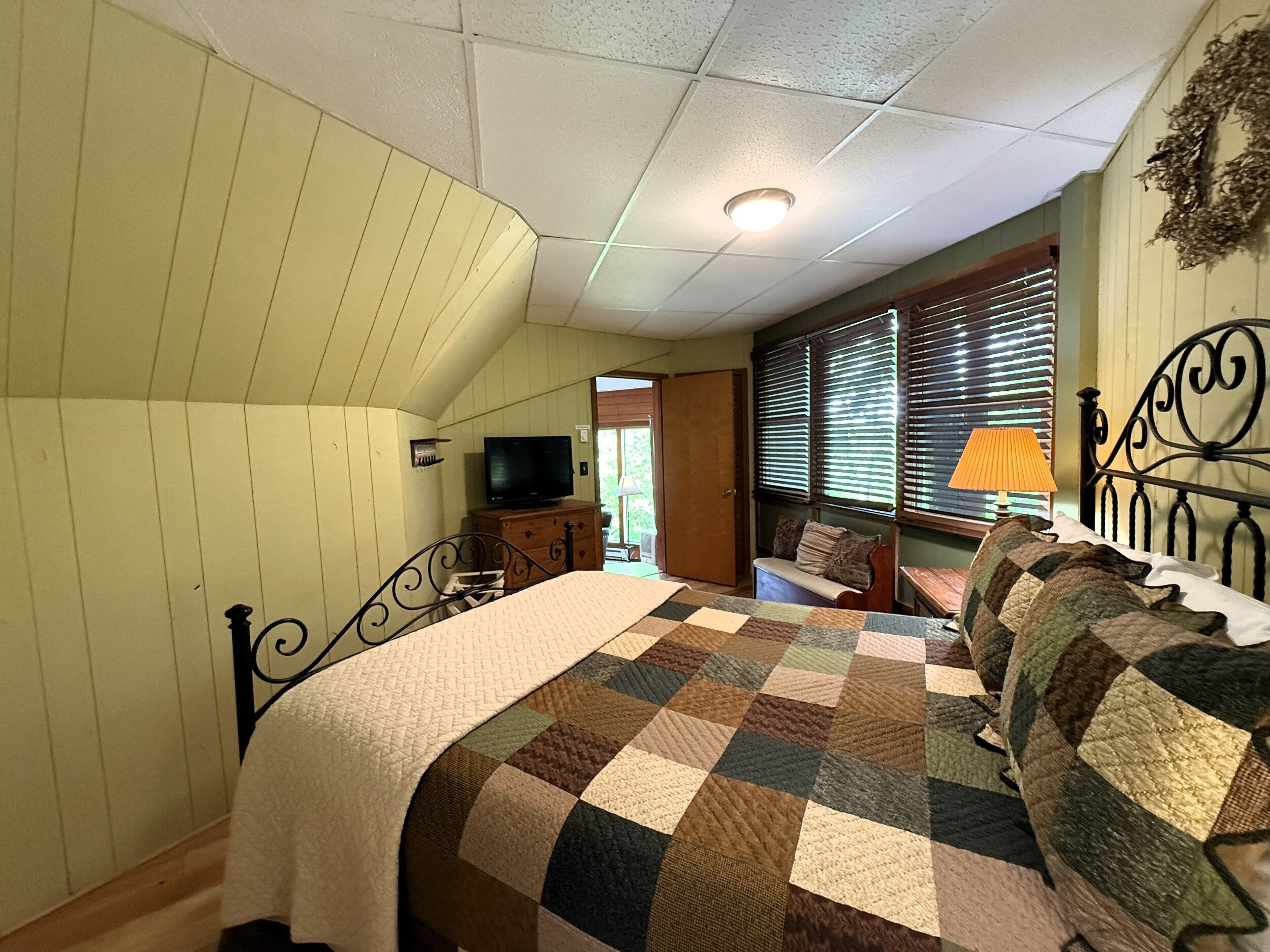 A bedroom with a bed, a television, a dresser, and a window with blinds.