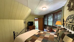 Een slaapkamer met een bed, een televisie, een dressoir en een raam met jaloezieën.