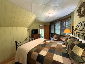 Ein Schlafzimmer mit Bett, Fernseher, Kommode und einem Fenster mit Jalousien.