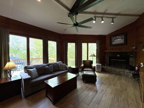Ein Zimmer mit einer Couch, einem Couchtisch, einem Sessel, einem Kamin und einem Deckenventilator.