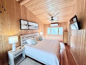 A wooden-paneled bedroom with a bed, bedside lamps, a ceiling fan, and a TV mounted on the wall. - Crystal Lake Retreat: Private Dock, Sauna, Parking, Firepit & 4BR (Gordon)