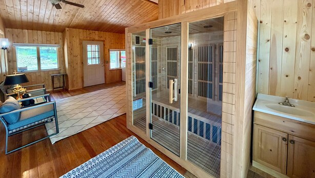 Ein Holzblockhaus-Innenraum mit Deckenventilator, einer Couch, einem Fenster und einer Glastür zum Balkon.