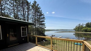 Eine Holzterrasse mit Geländer, die auf einen See mit umliegenden Bäumen blickt.