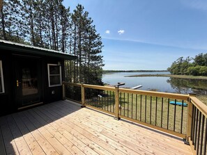 A wooden deck with a railing overlooking a lake, surrounded by trees. - Crystal Lake Retreat: Private Dock, Sauna, Parking, Firepit & 4BR (Gordon)