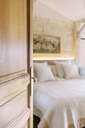 Eine Holztür führt in ein Schlafzimmer mit einem Bett, Kissen und einem Bild an der Wand.