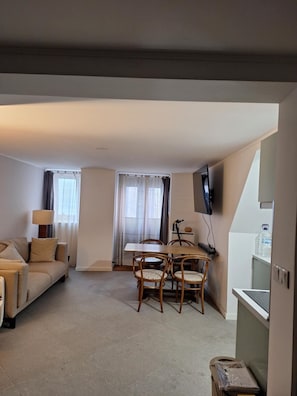 Een woonkamer met een bank, een eettafel met stoelen, een aan de muur bevestigde televisie en een waterdispenser.