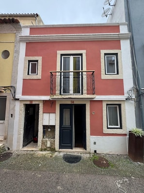 A two-story building with a balcony, a black door, and a small window on the ground floor.