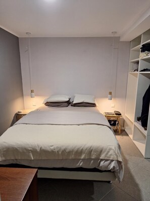 Een minimalistische slaapkamer met een bed, nachtkastjes en een garderobe.