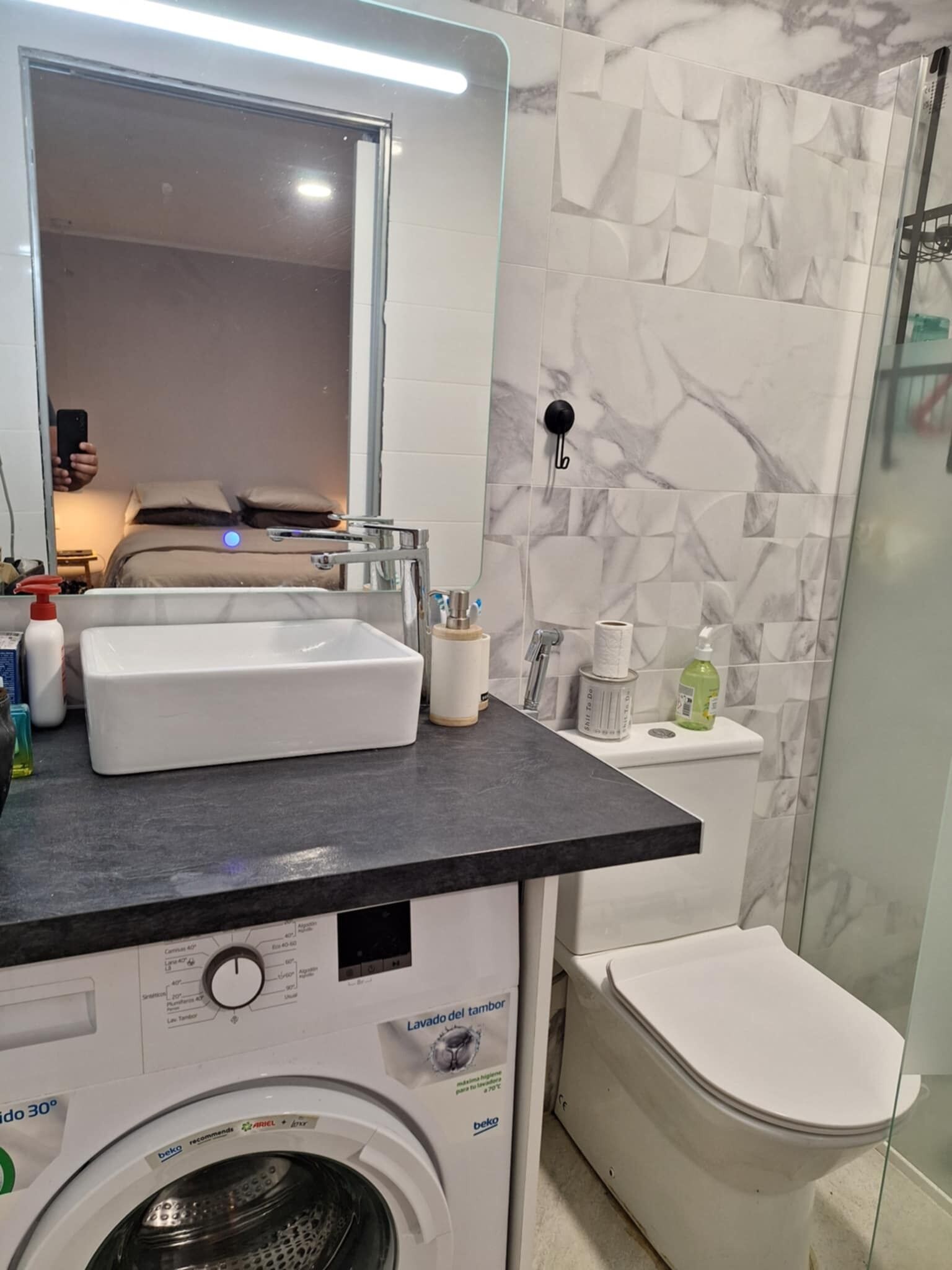 A bathroom with a washing machine, a sink, a toilet, and a mirror.
