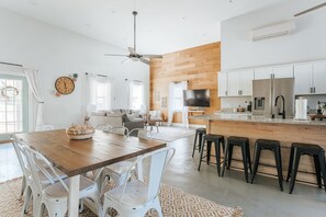 Una cocina moderna con una isla de madera, taburetes blancos y un televisor de pantalla plana.