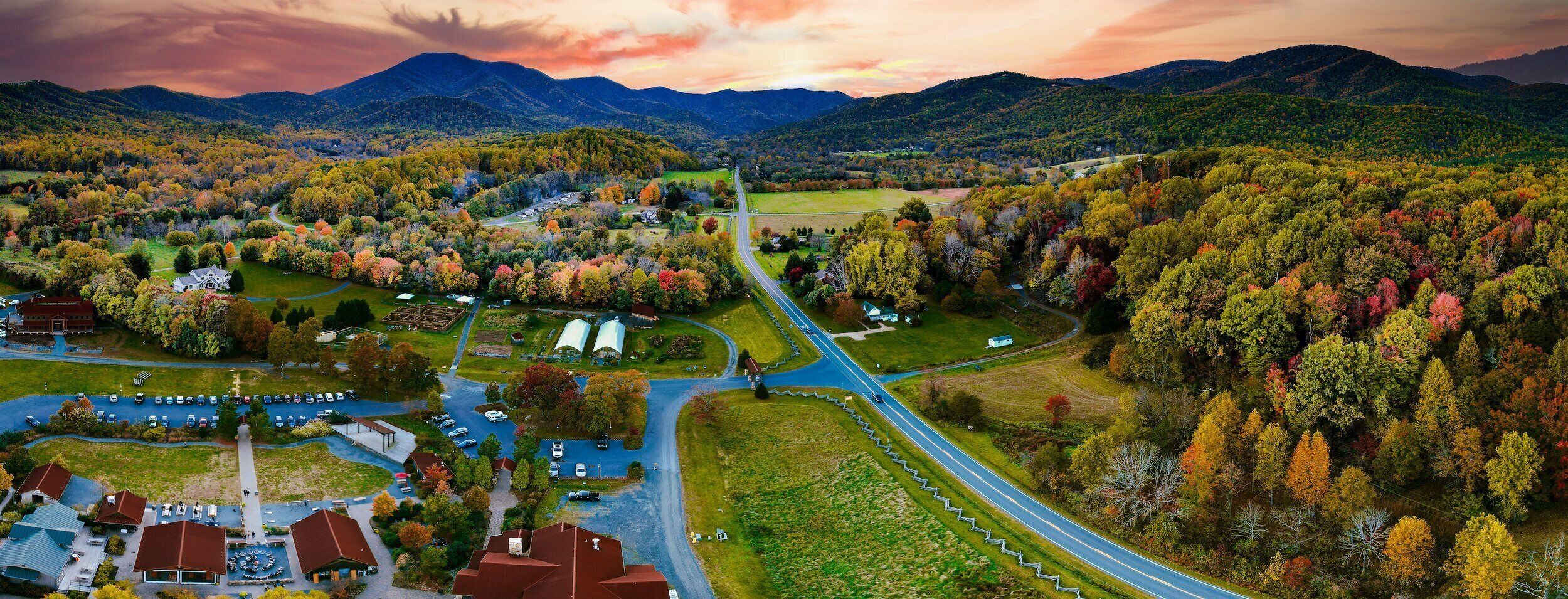 A rural landscape with a road, buildings, and autumn foliage.