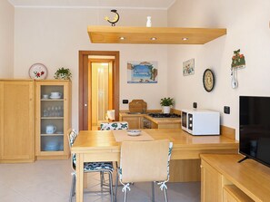 A compact kitchen with a dining area, wooden cabinets, a microwave, and a television. - Coniglio Beach by Interhome (Villasimius)