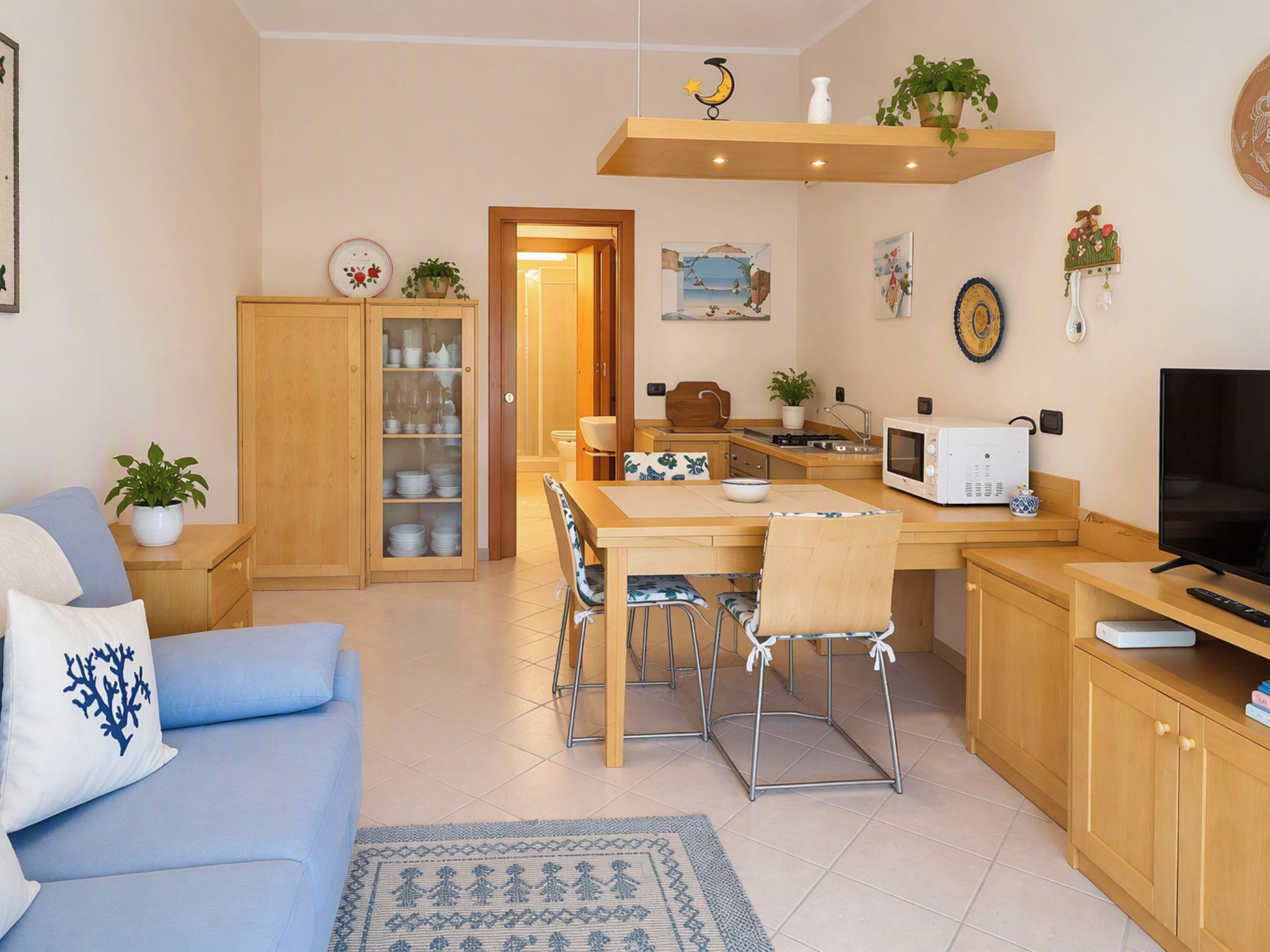 Ein modernes Wohnzimmer mit Sofa, Esstisch, Stühlen, Fernseher und einer Küchenzeile mit Mikrowelle und Spüle.