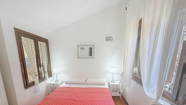 Une chambre à coucher avec un lit, deux tables de chevet, un miroir et une fenêtre avec des rideaux.